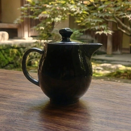 A glossy black ceramic teapot with a lid.